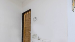 Een badkamer met een wit wastafelmeubel, een houten deur en een betegelde vloer.
