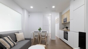 A modern kitchen with white cabinets, a dining table with chairs, a grey sofa with striped pillows, and a TV on a wooden stand. - Ría De San Cosme María Apartment with Mountain Views, Shared Garden & Air Conditioning (San Cosme-Outes)