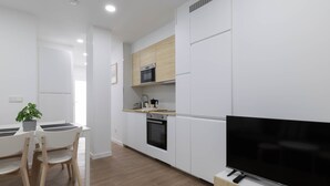 A modern kitchen with white cabinets, a microwave, an oven, and a flat-screen TV on a wooden stand. - Ría De San Cosme María Apartment with Mountain Views, Shared Garden & Air Conditioning (San Cosme-Outes)