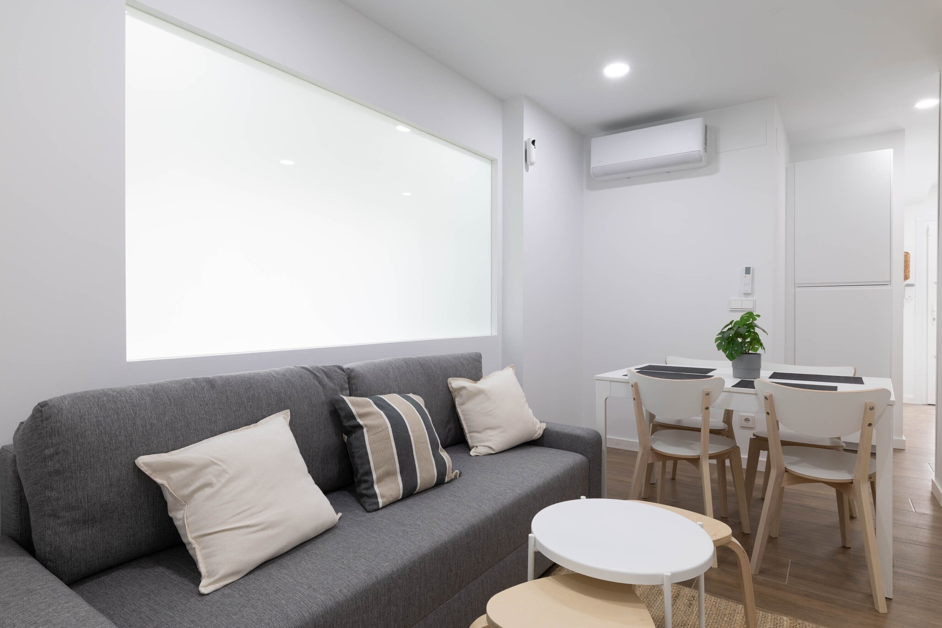 A modern living room with a grey sofa, a round table, and a dining area with chairs.