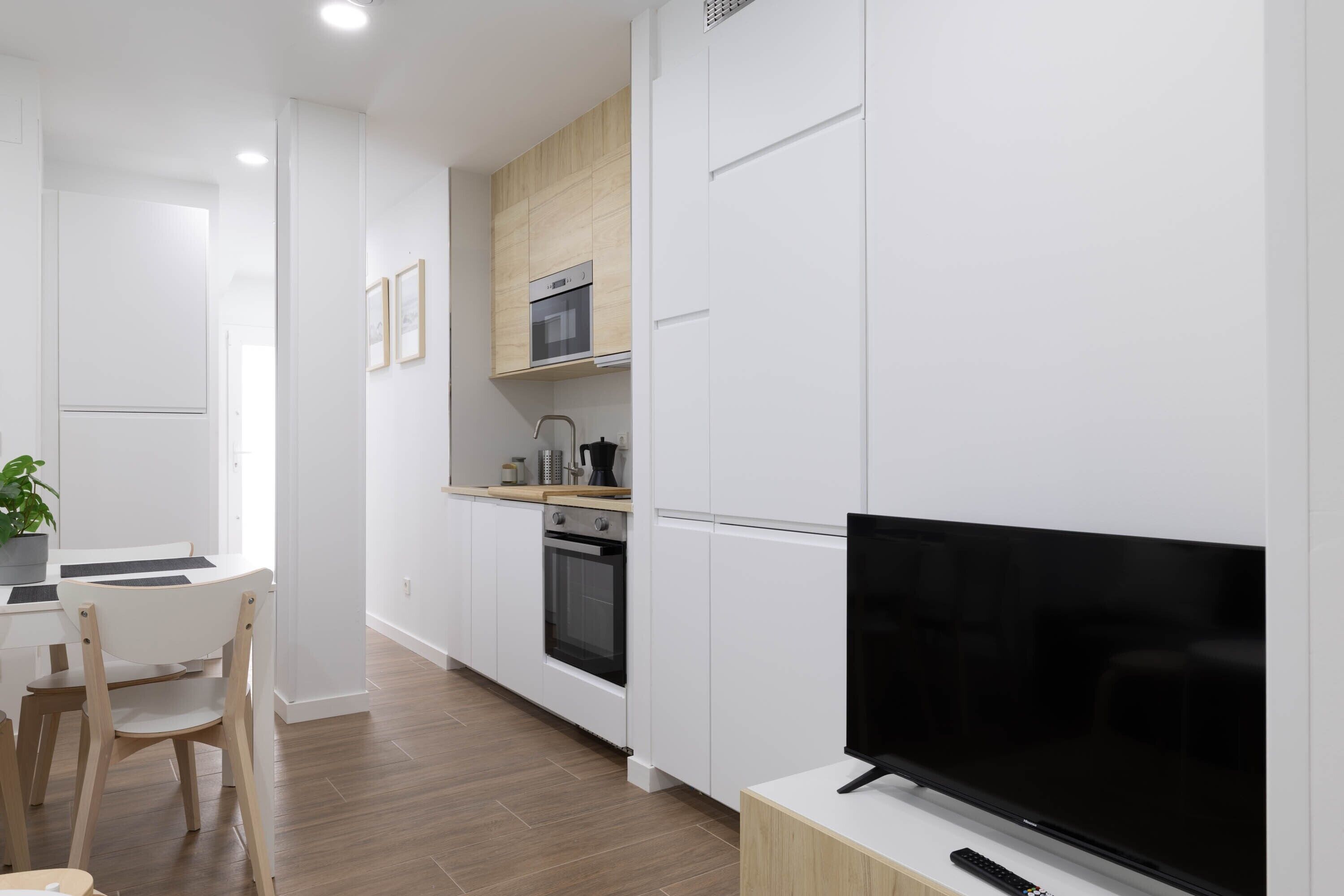 Une cuisine moderne avec des armoires blanches, un four encastré et un téléviseur à écran plat posé sur un meuble en bois.