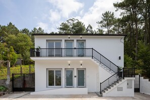 A modern two-story building with a balcony, a staircase, and a gated entrance. - Candida Apartment with Mountain Views, Shared Garden, and Air Conditioning (San Cosme-Outes)