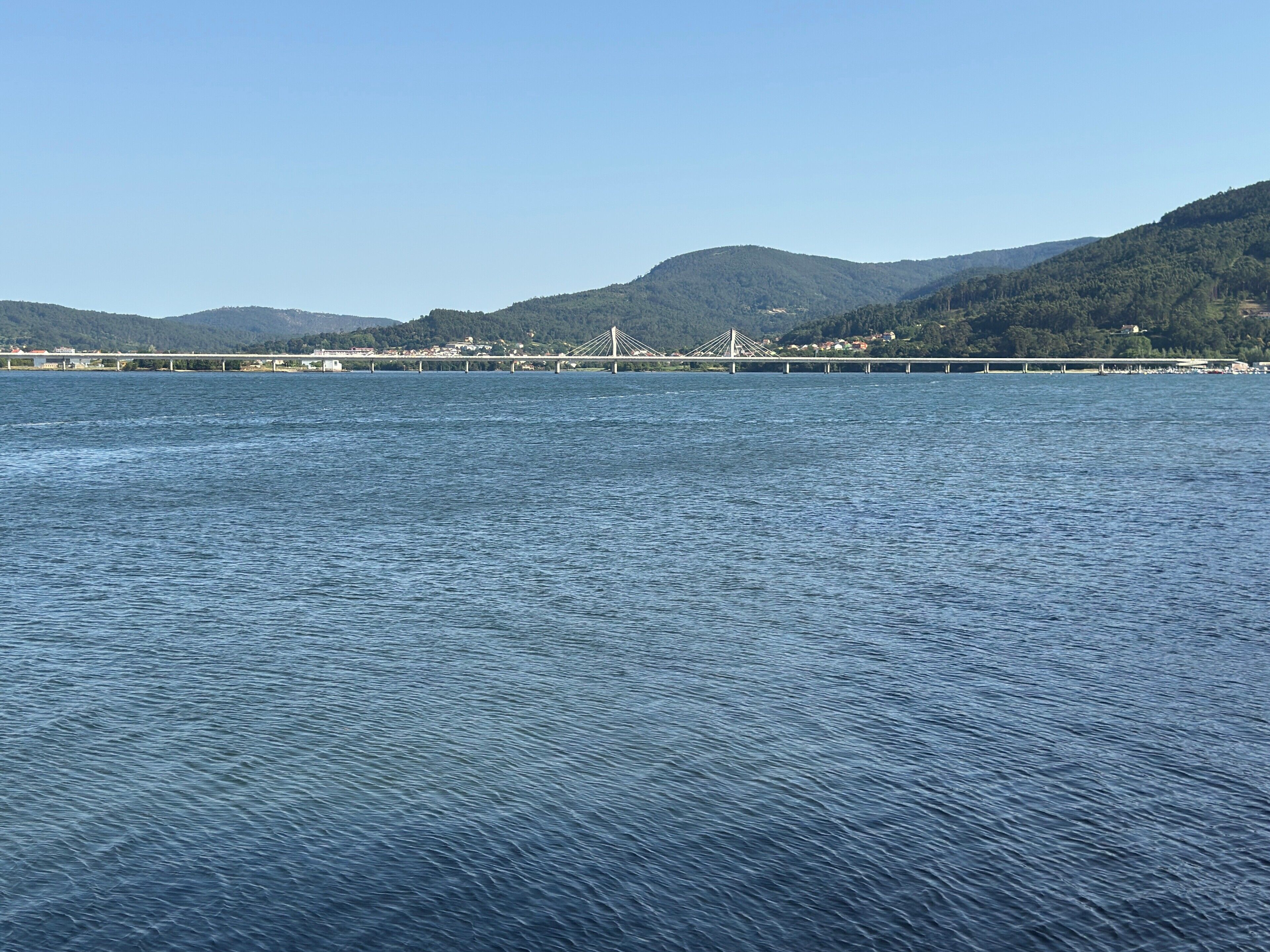 A large body of water with a bridge spanning across it, surrounded by hills.