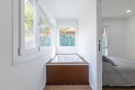 A modern bathroom with a wooden bathtub, a window, and a door leading to a bedroom.. Ría De San Cosme Laxeira Apartment with Mountain Views, Shared Garden & Air Conditioning