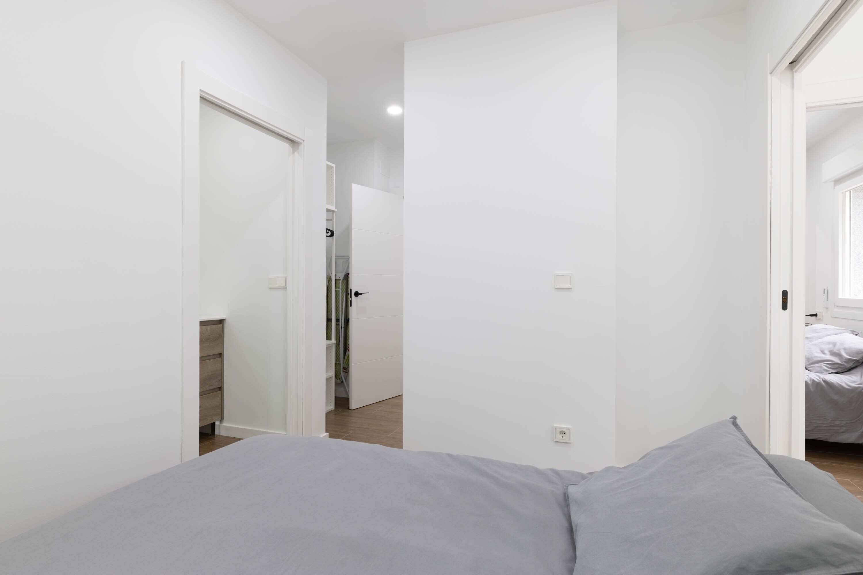 Een smalle gang die leidt naar een slaapkamer met een bed en een deur.