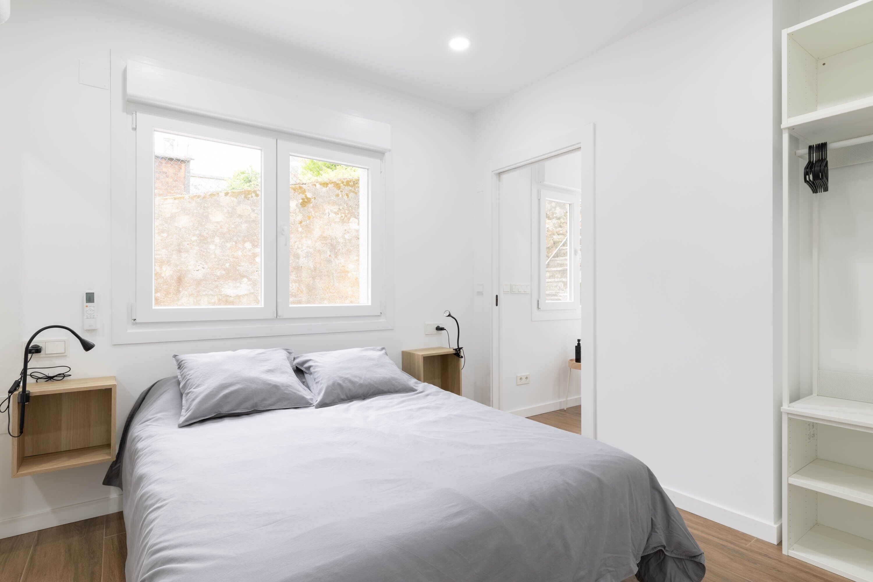 A bedroom with a bed, a window, a bedside table, and a wardrobe.