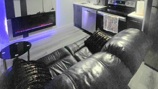 A modern living room with a leather sofa, a flat-screen TV, and a kitchen area with a stove and microwave. - Discover your ideal getaway. Relax and recharge in a space that feels like home. (Edmonton)