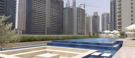 A modern urban setting with high-rise buildings, a swimming pool area with steps, and construction cranes in the background.