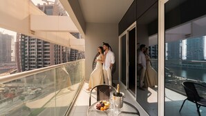 A balcony with a table set for two, a bottle of champagne, and a glass of wine. - Keyrock Living - 1BR Lake View at Reva (Dubai)