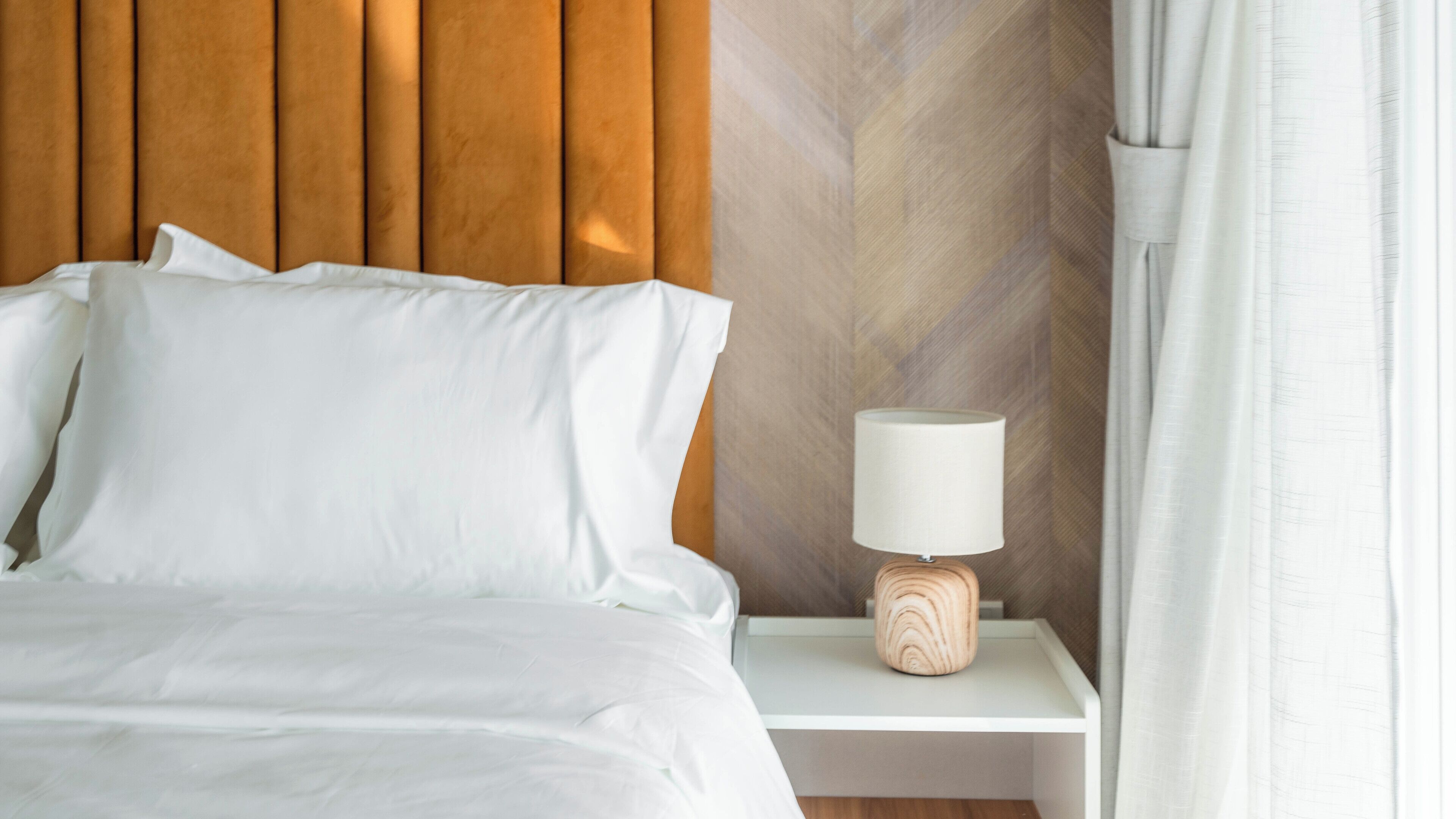 A neatly made bed with white linens, a wooden headboard, and a bedside table with a lamp.