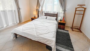 Un dormitorio ordenado con una cama grande, una mesita de noche con lámpara, un espejo de pie y una lámpara de pie.
