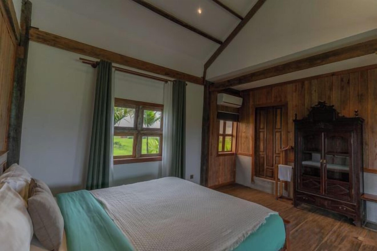 A bedroom with a bed, a window, a wardrobe, and a door leading to another room.