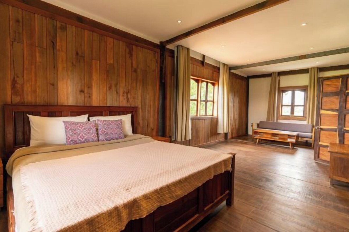 Une chambre spacieuse avec un grand lit, des murs en bois et une fenêtre laissant entrer la lumière naturelle.