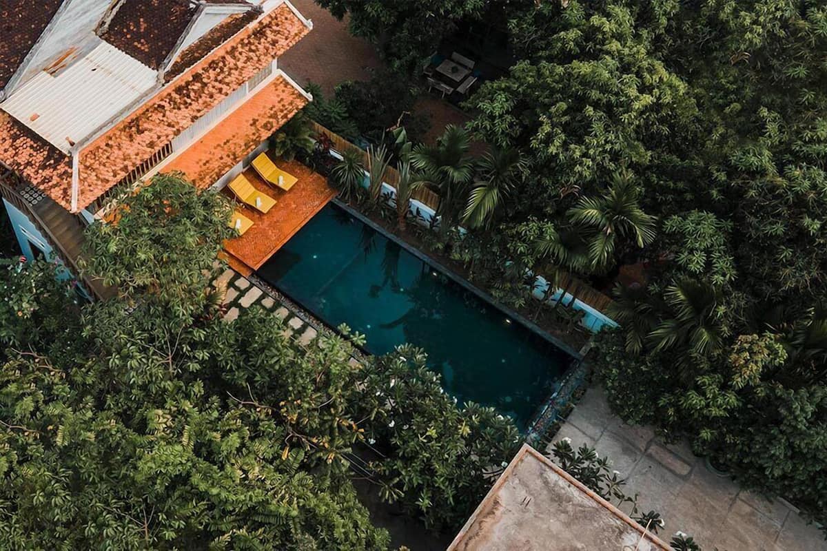 An aerial view of a property with a swimming pool surrounded by lush greenery and a patio area with yellow seating.