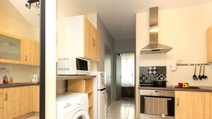 A modern kitchen with wooden cabinets, a washing machine, a microwave, a refrigerator, a stove, and hanging utensils.