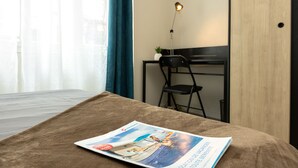 A hotel room with a bed, a desk, a chair, and a window with curtains.