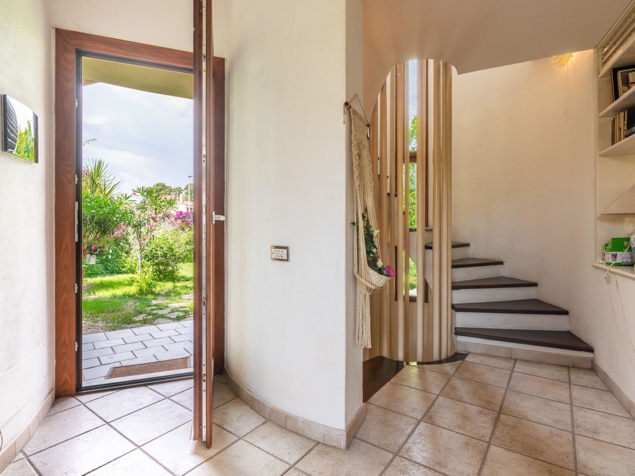 Eine Treppe mit Wandbehang aus Makramee, eine Tür, die in einen Garten führt, und ein Regal mit Gegenständen.