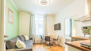 Un espace de vie compact comprenant un canapé, une table à manger avec des chaises, une machine à café et un téléviseur fixé au mur.