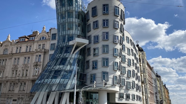 Un bâtiment moderne à la façade en verre et un bâtiment traditionnel à l’architecture classique.