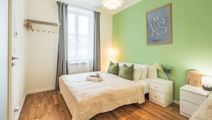 Une chambre à coucher comprenant un lit, des tables de chevet, une commode, une fenêtre avec des rideaux, un luminaire suspendu et une œuvre d’art accrochée au mur.