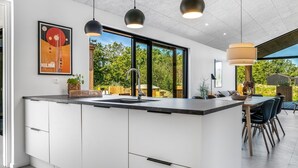 A modern kitchen with a large island, pendant lights, and a view of the outdoors.