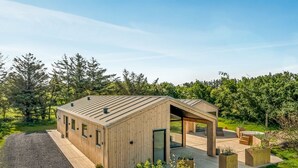 A modern wooden cabin with a deck, surrounded by lush greenery and trees.