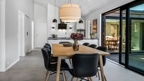 A modern dining area with a wooden table and black chairs, a large pendant light, and a view of the outdoors through large windows.