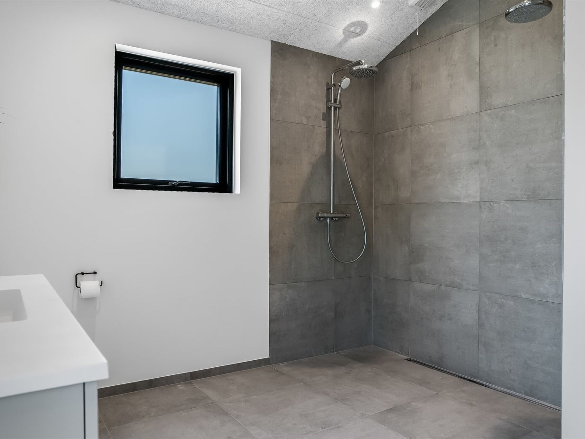 Ein modernes Badezimmer mit Dusche, Fenster und Waschbecken.