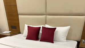 Un lit bien fait, recouvert d’une courtepointe blanche et rouge à motifs, avec une tête de lit rembourrée de couleur beige et un mur recouvert de panneaux de bois.