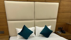 Un lit bien fait, recouvert d’une courtepointe turquoise à motifs, avec deux oreillers turquoise, une tête de lit en bois et une table de chevet sur laquelle se trouvent un téléphone et une télécommande.