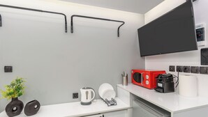 Una cocina moderna con encimera blanca, un hervidor, un tostador rojo, una cafetera negra y un televisor de pantalla plana montado en la pared.