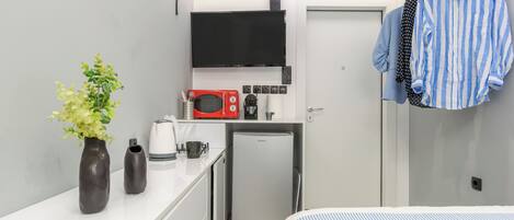 Una habitación de hotel compacta con kitchenette, una cama con ropa de cama a rayas y un perchero.