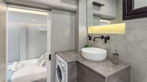 Un baño moderno con lavadora integrada, un lavamanos redondo y un espejo con luz superior.