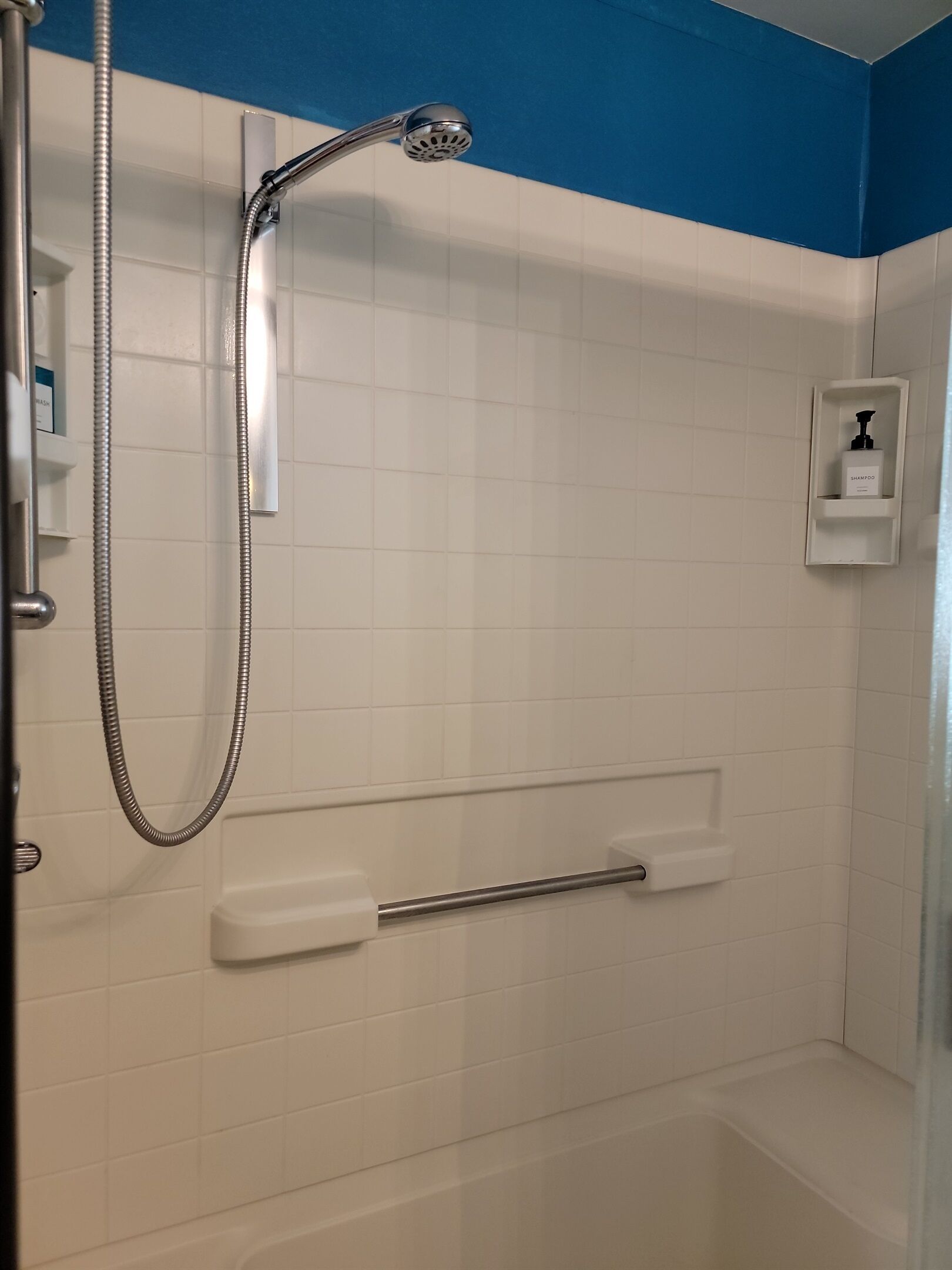 A shower with a handheld showerhead, a handheld shower attachment, and a soap dispenser on the wall.