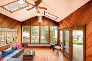 Une pièce chaleureuse avec un plafond en pente, des murs en bois, un ventilateur de plafond, de grandes fenêtres, un canapé, une table et une chaise.