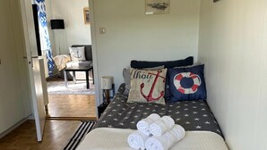 A bedroom with a bed, pillows, a bedside table, a lamp, and a view into another room. - Scenic by the sea Patterdale Apartments (Gamleby)