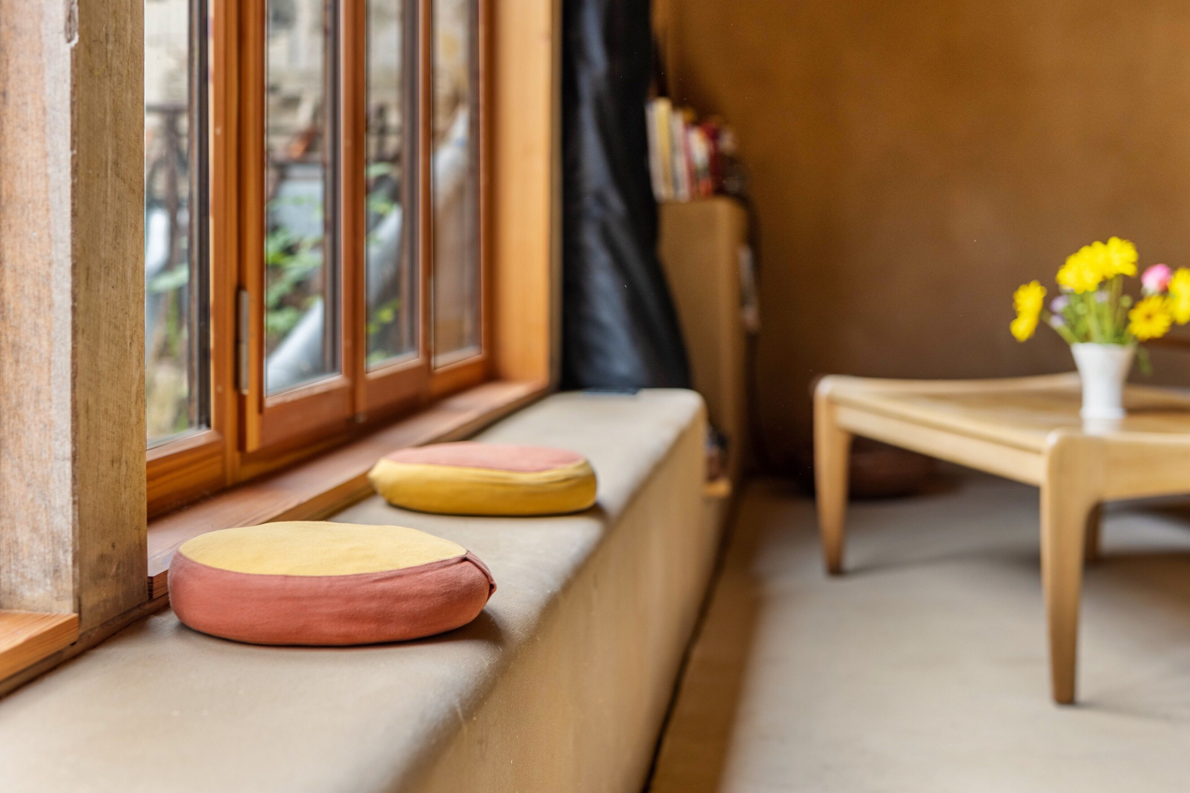 Ein Zimmer mit Fensterbank, einem kleinen Tisch mit Blumenvase und einem Bücherregal.