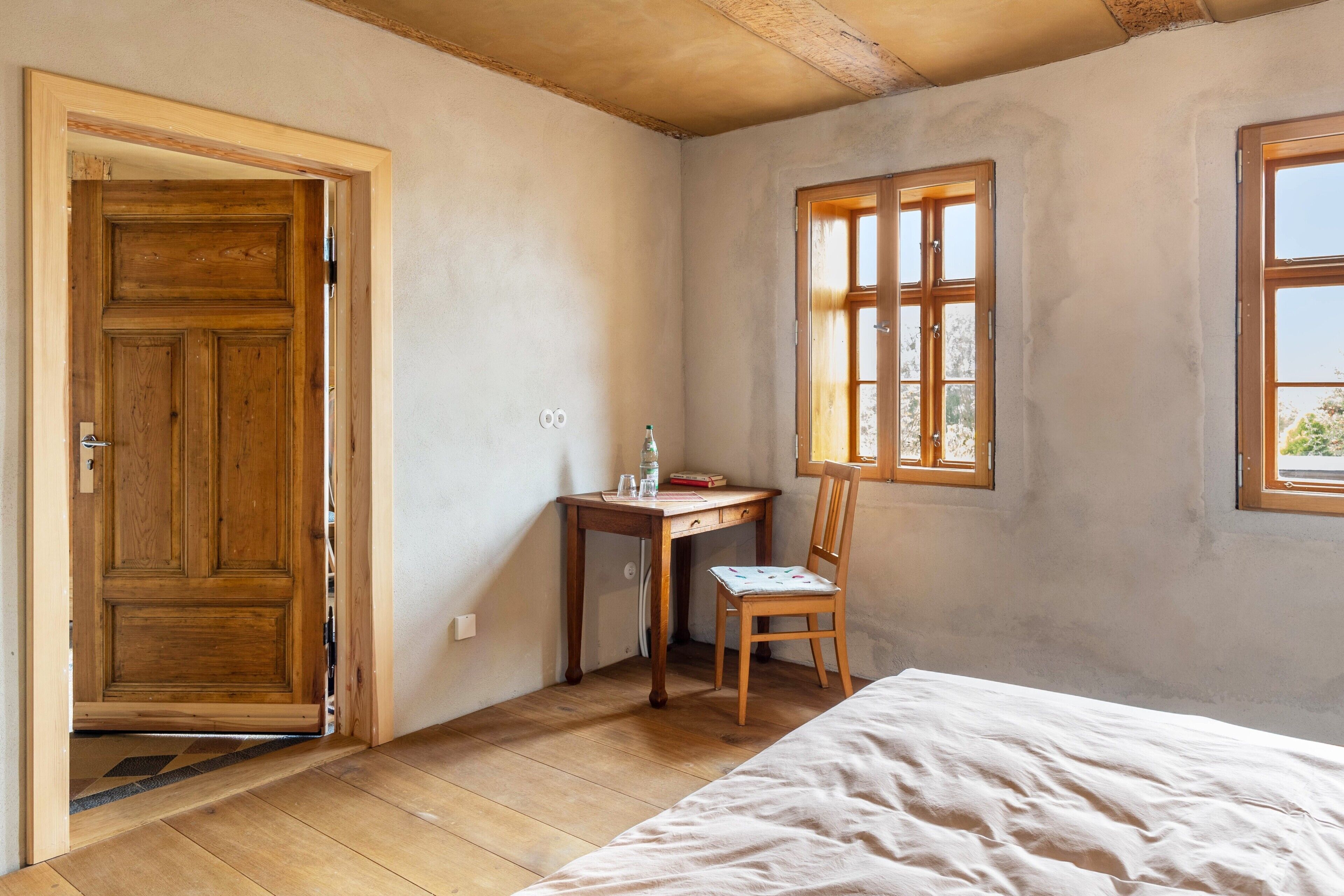 Una habitación con puerta de madera, un escritorio con silla, una cama y una ventana.