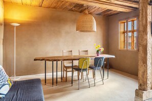 A rustic dining area with a wooden table, chairs, a hanging light fixture, and a window with a view.