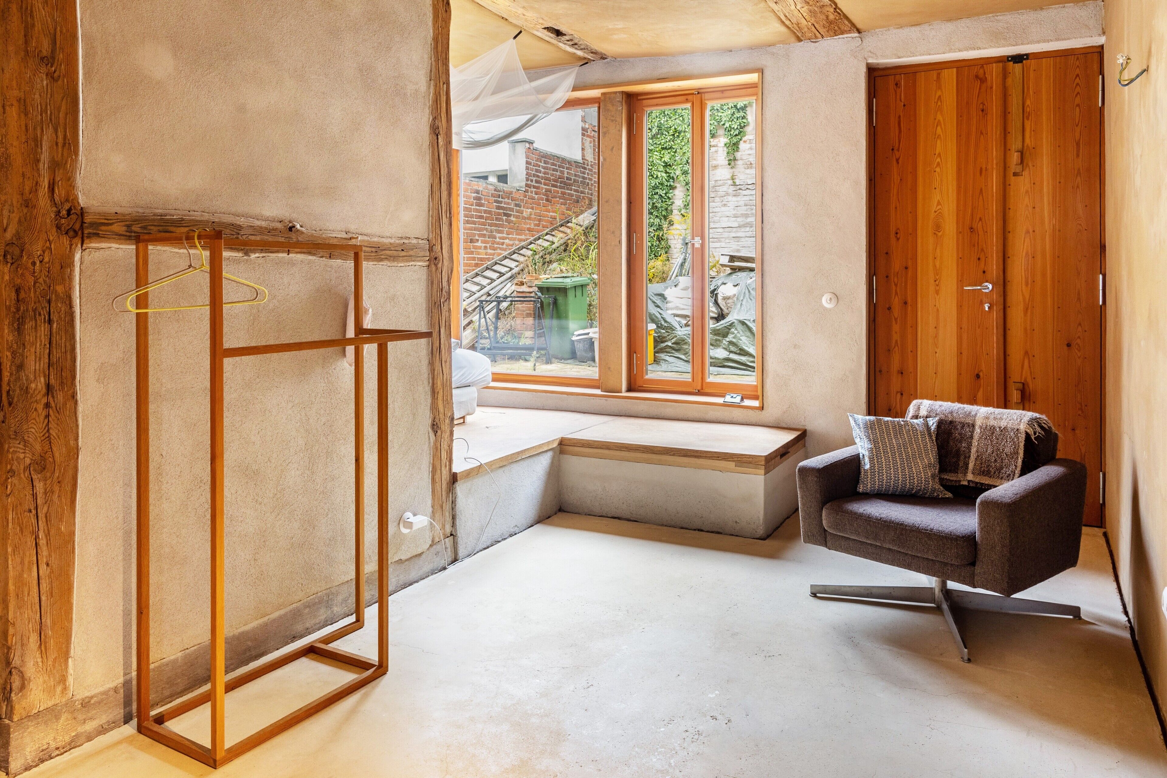 A room with a wooden floor, a bench, a chair, and a wooden door.