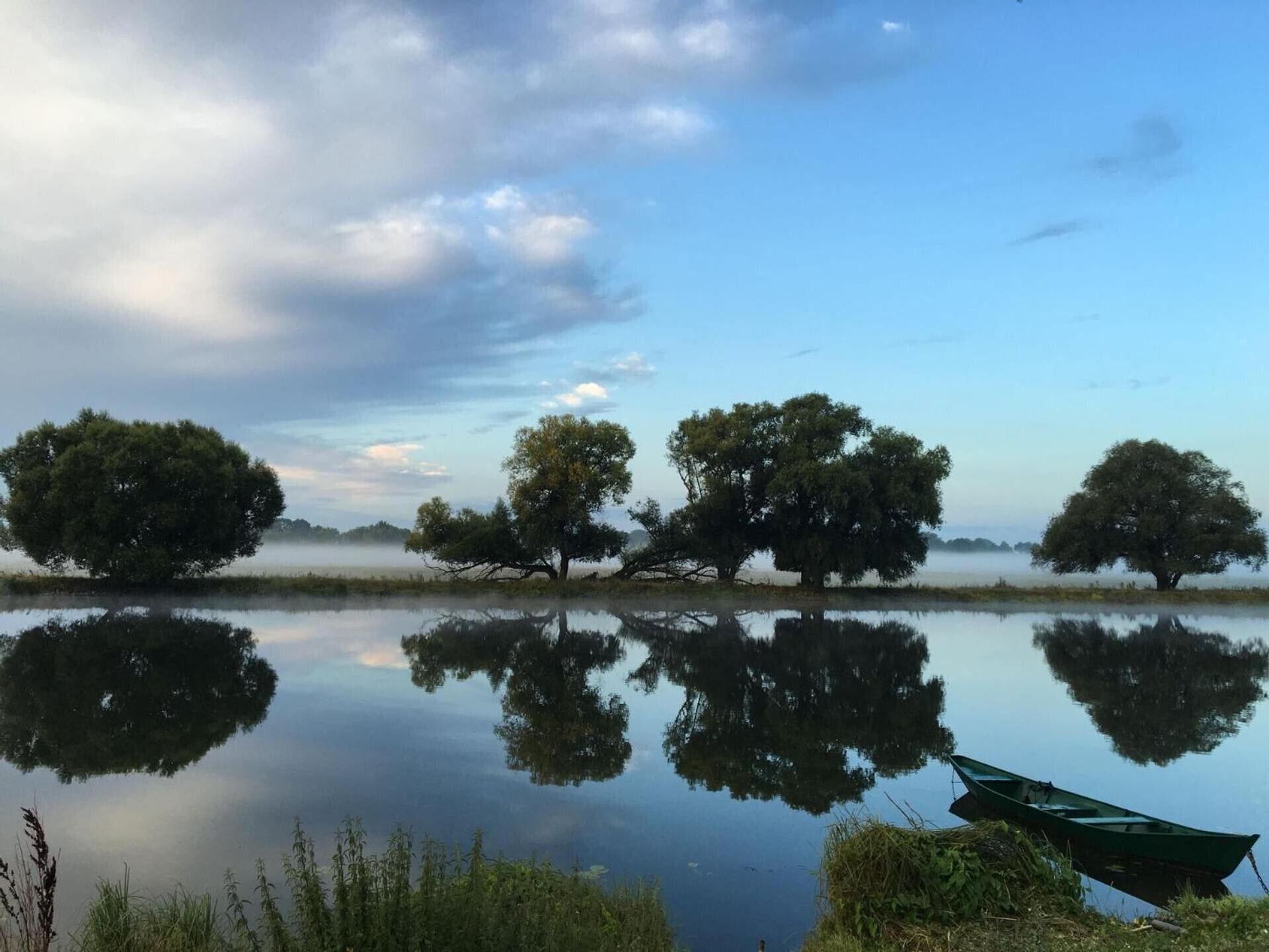 A calm lake with trees reflecting on the water, a boat, and a misty atmosphere.