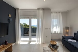 A modern living room with a dark wall, a flat-screen TV, a sofa, a coffee table, and a large window with curtains.