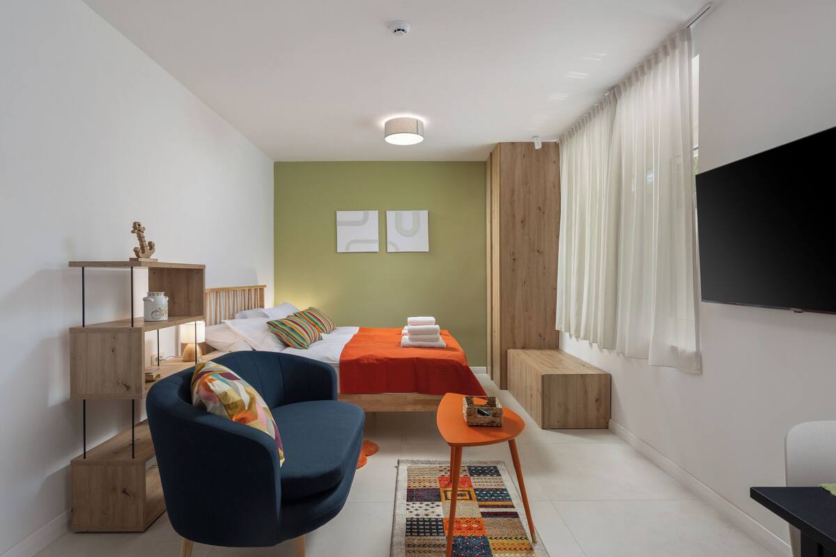 Un dormitorio moderno con una cama, una silla, una mesita, un televisor y un armario de madera.
