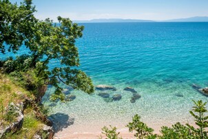 A coastal landscape with clear turquoise waters, rocky shoreline, and lush greenery.