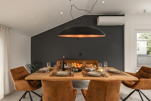 A modern dining area with a wooden table set for six, surrounded by leather chairs, a black pendant light, and a dark accent wall. - Desamani 975 Apartments (Kostrena)