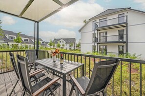 A balcony with a table and chairs, a bottle of wine, and a vase of flowers.