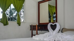 A hotel room with a bed, a wooden nightstand, a mirror, and green curtains. - Mami Resort (Tangalle)