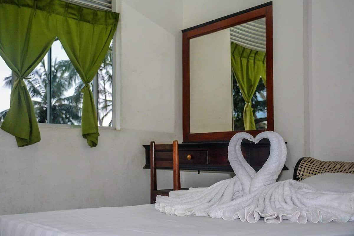 A hotel room with a bed, a wooden nightstand, a mirror, and green curtains.