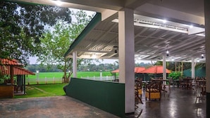 An outdoor covered area with tables and chairs, a view of a green field, and a white fence. - Mami Resort (Tangalle)