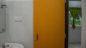 A bathroom with a white sink, a mirror, and a door leading to a shower area with a green curtain. - Mami Resort (Tangalle)